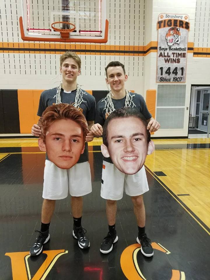 Two Strasburg Tigers male athletes in a gym holding cardboard cut out fat heads of their faces.