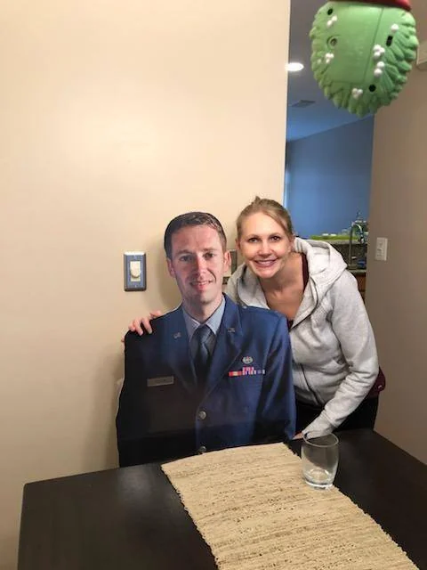 Woman with a standup fat head cardboard cut out of a man in uniform.